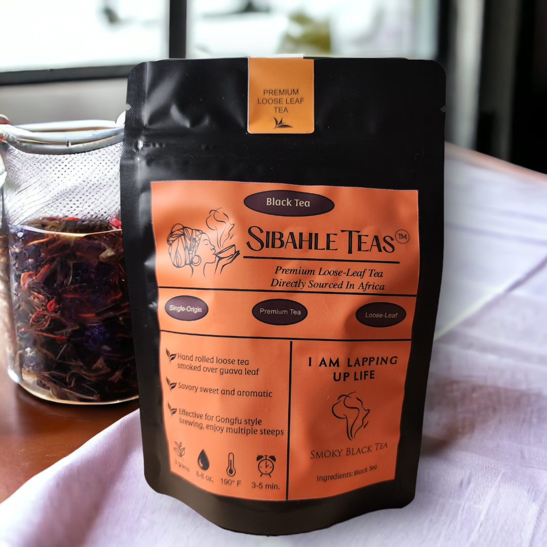 I Am Lapping Up Life, a smoky black tea is pictured in a black stand-up pouch.  The product label is orange and contains product descriptors and instructions for how to brew the tea.  The orange label has the name of the business, Sibahle Teas, and a logo image of a woman with a headwrap sipping tea from a bowl and steam rising from her cup in the shape of Africa.